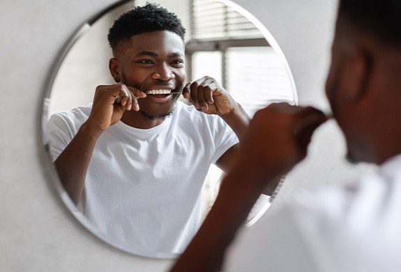 Man smiling while flossing in mirror